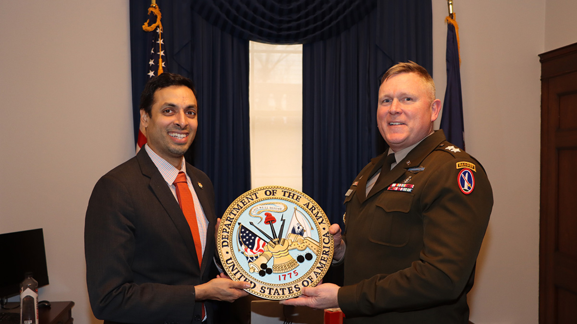 Congressman Suhas Subramanyam and a uniformed Army officer stand side by side, jointly holding a decorative Department of the Army seal plaque.