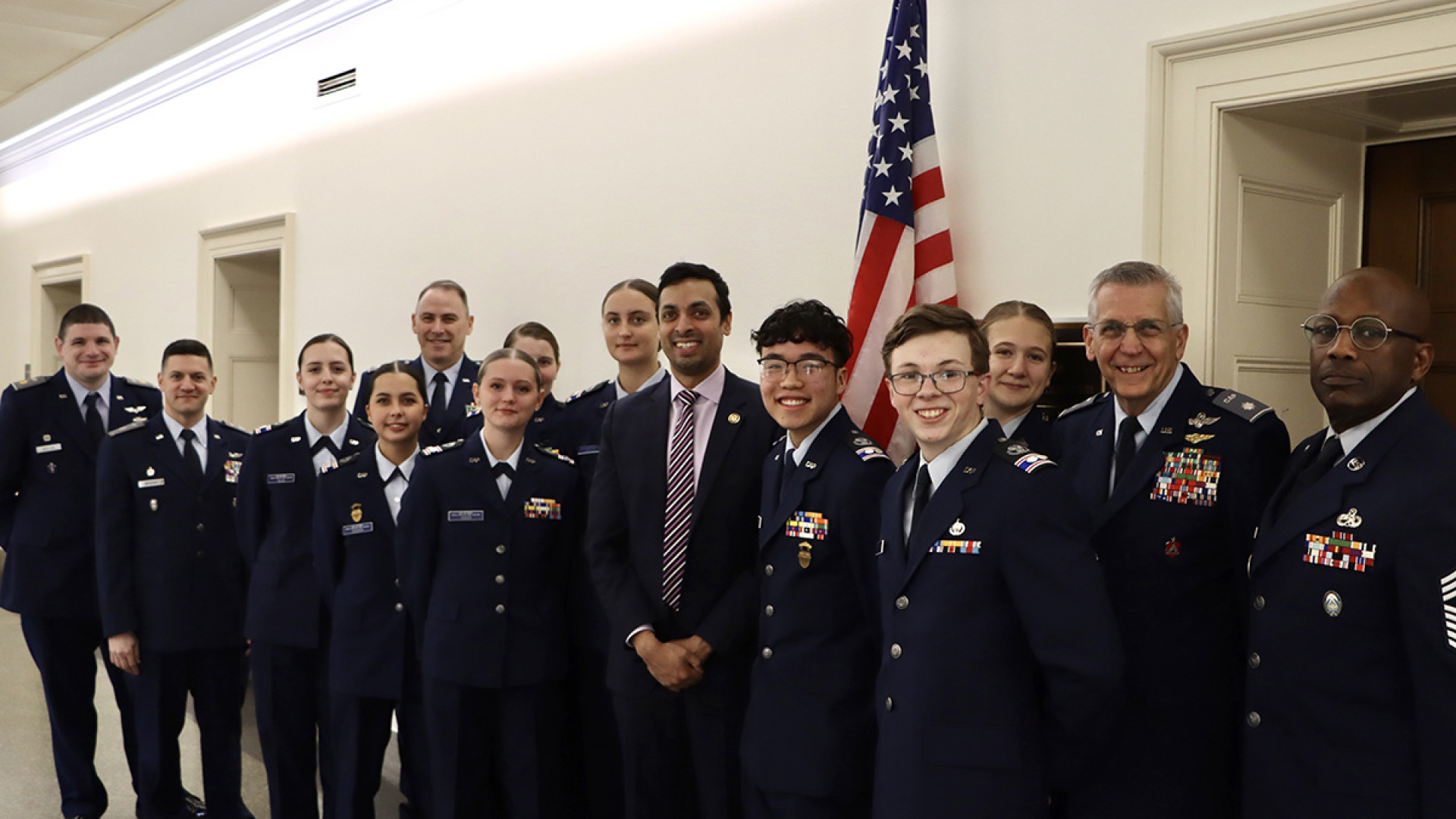 Congressman Suhas Subramanyam stands alongside Civil Air Patrol cadets and senior officers in uniform, posed in a hallway by an American flag.