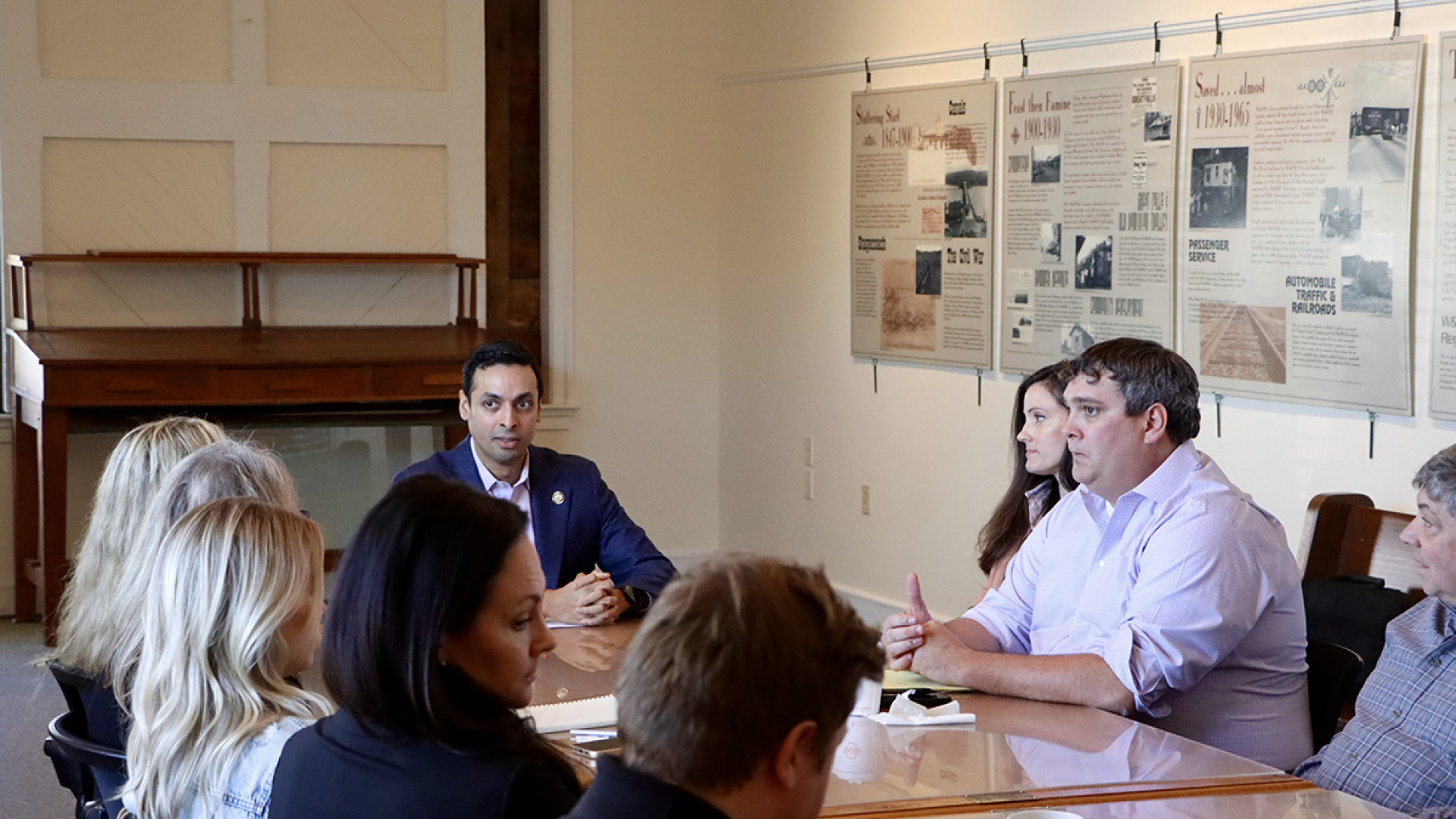 Congressman Suhas Subramanyam sits at a conference table in a gallery-like room, attentively listening as constituents share their concerns.
